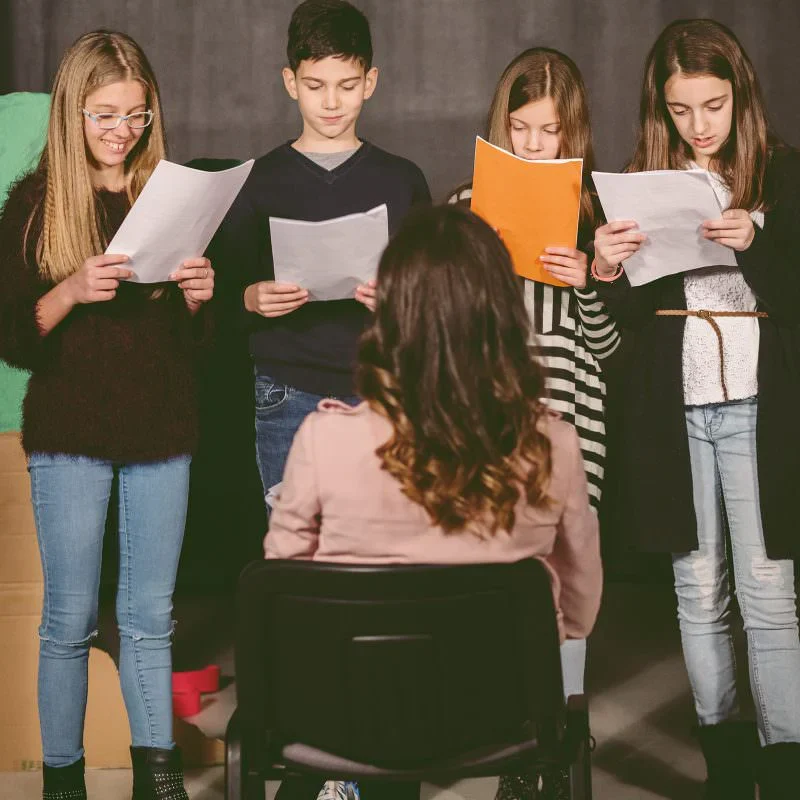 Students rehearsing scripts before teacher